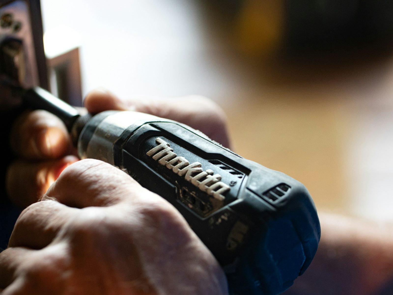 Locksmith's hand driving a cordless drill into the edge of a dark entry door while fitting new lock hardware