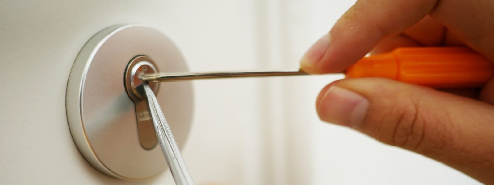 Close-up of a lock cylinder being opened with a tension tool and a screwdriver on a white door