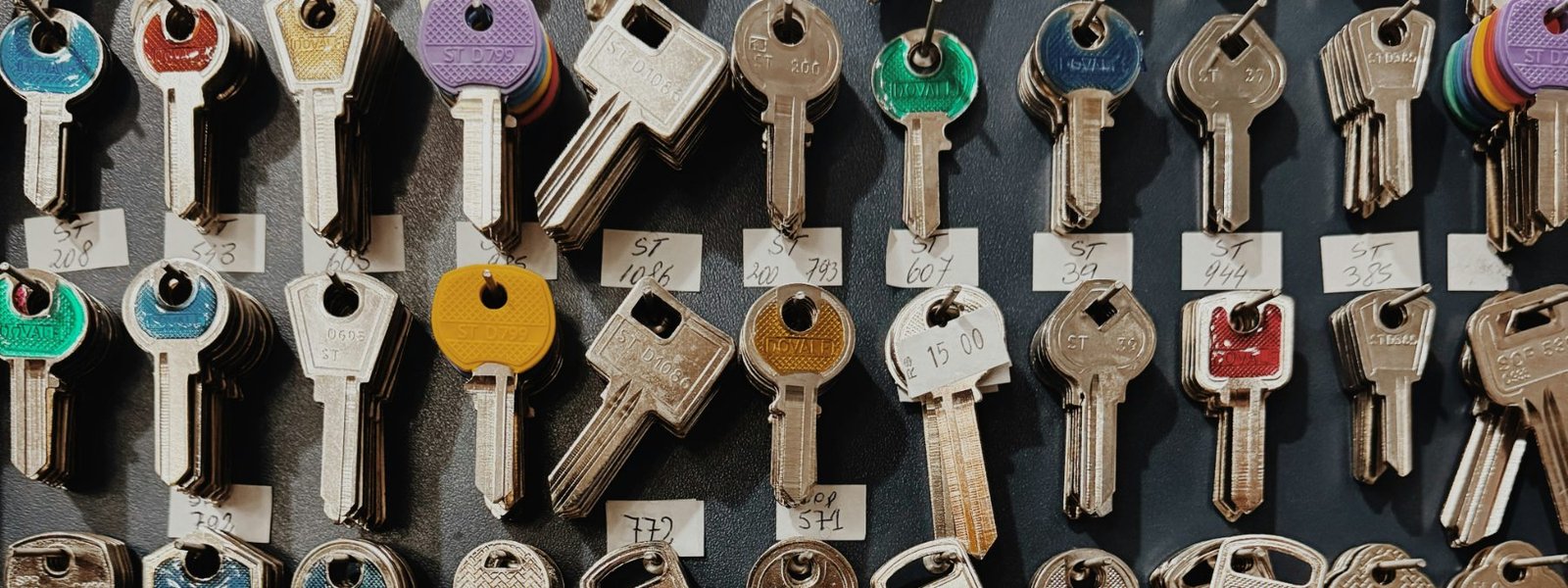 Wall display of labelled key blanks hanging in rows, many with coloured plastic heads