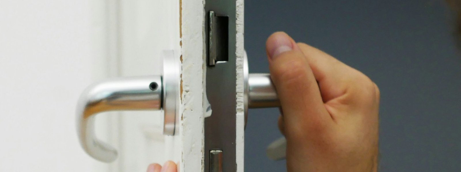 Lever handle and mortise lock faceplate on a door edge being set in place by hand