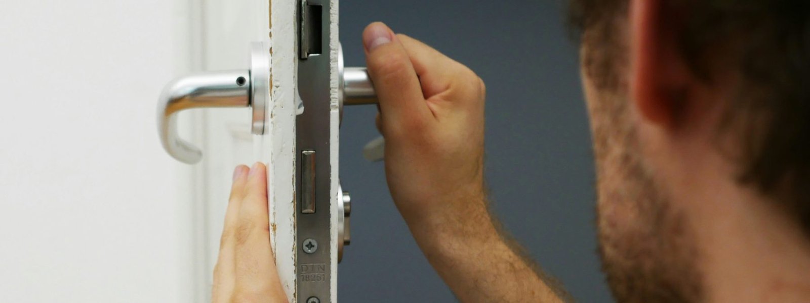 Technician fitting a mortise lock and lever handle into a white interior door