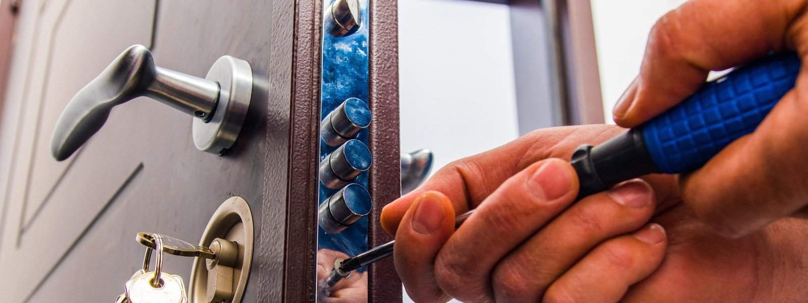 Row of steel deadbolt bolts along the edge of a security door, with a bunch of keys hanging from the cylinder