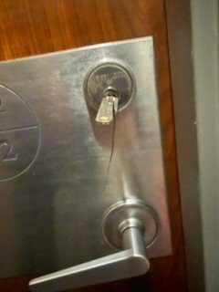 Key in a lock cylinder above a steel lever handle on a commercial door