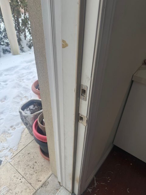 Edge of an exterior door and its frame, with the latch and strike checked for alignment