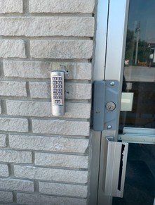 Mechanical keypad lock installed on a commercial door beside a brick wall
