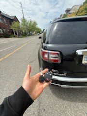 Two replacement remote keys held beside a black SUV parked on the street